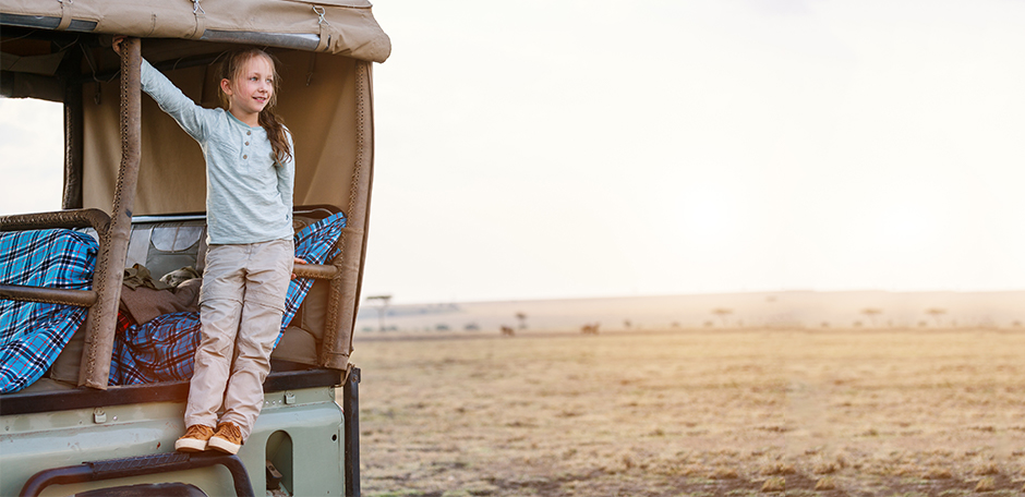 A young girl stands on the vehicle on a family vacation in Kenya